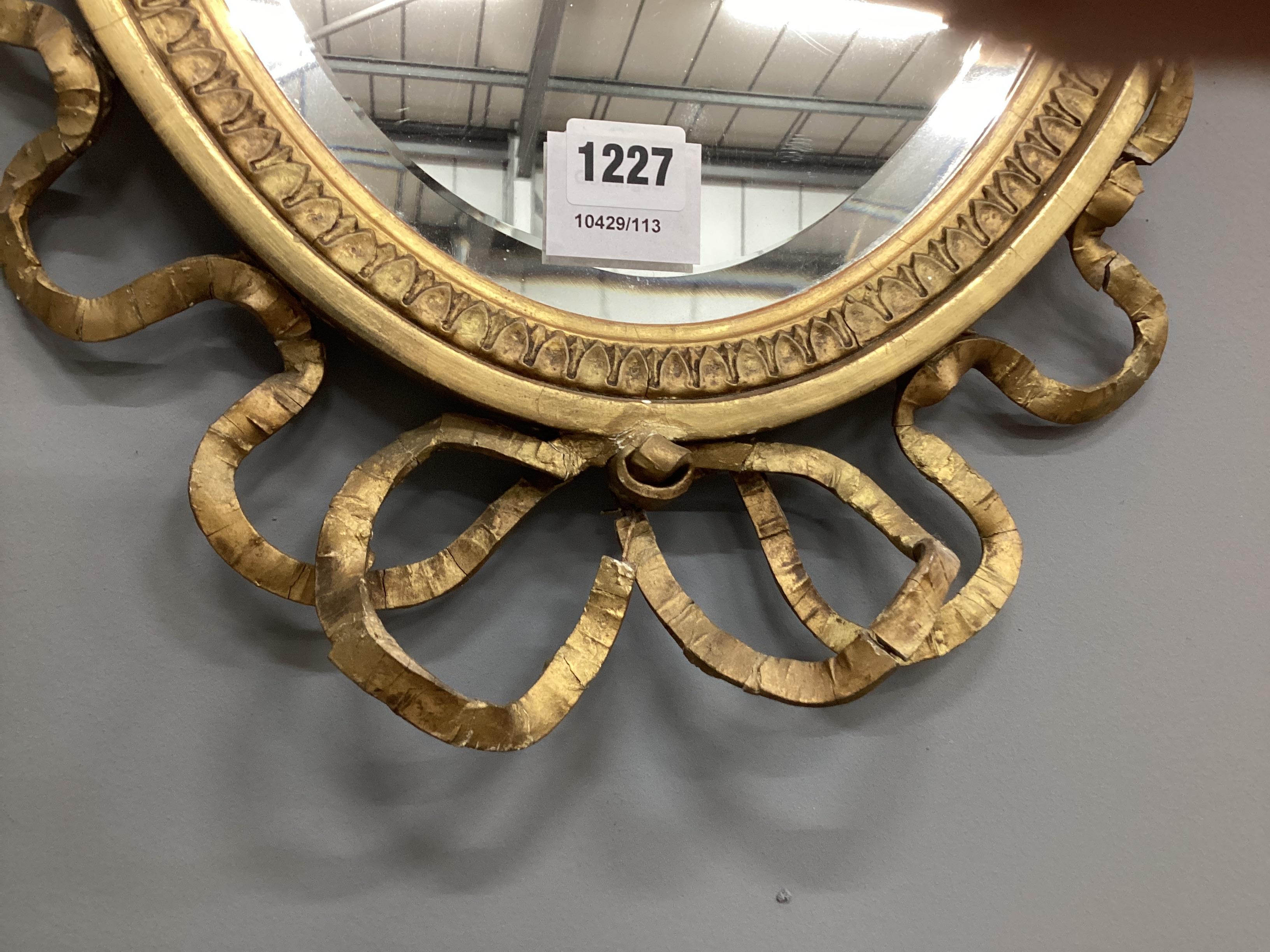 An Edwardian oval giltwood and composition swagged urn and ribbonfold wall mirror, width 41cm, height 76cm.
